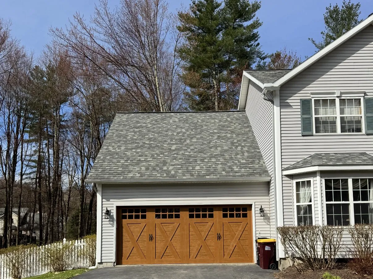 Wood-look cross-buck carriage garage door on a grey-sided attached garage