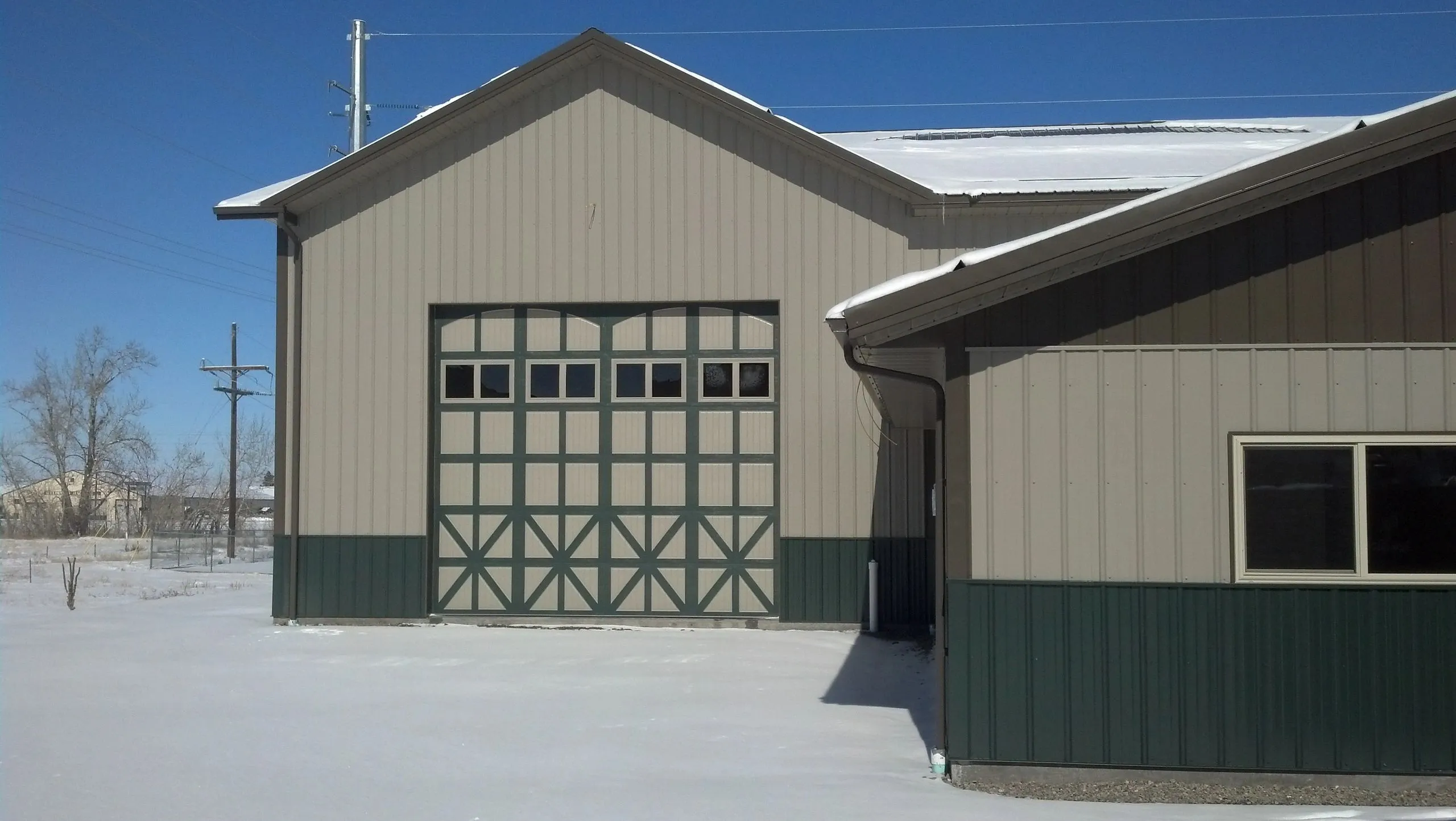Decorative cross-buck overhead door on a tan and green steel building in winter