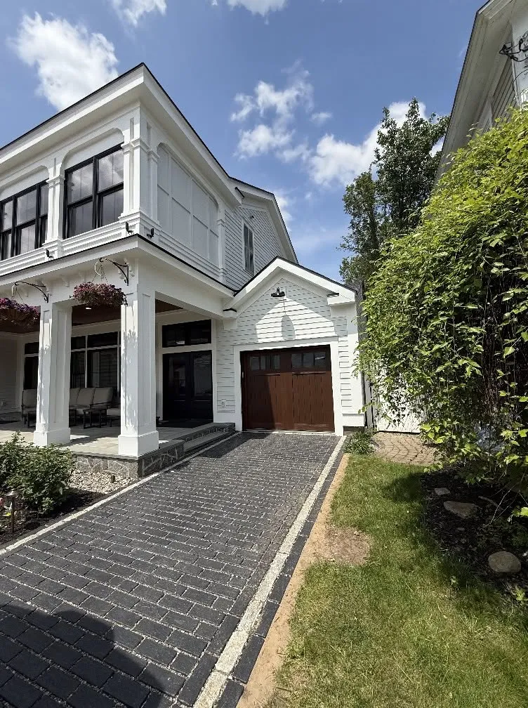 Single wood carriage-style garage door on a white home with a paver driveway