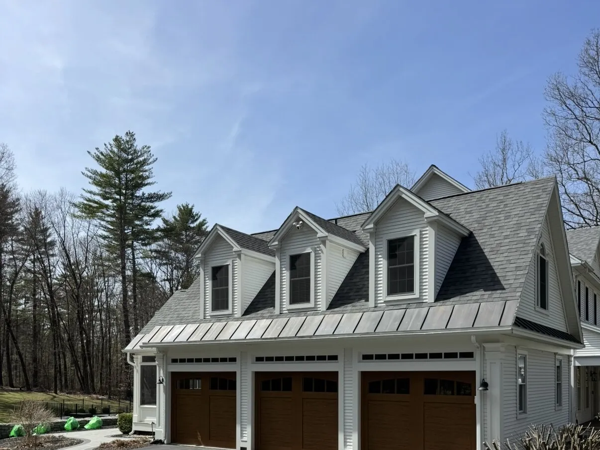 Three wood-look carriage-style garage doors under dormers on a white clapboard home